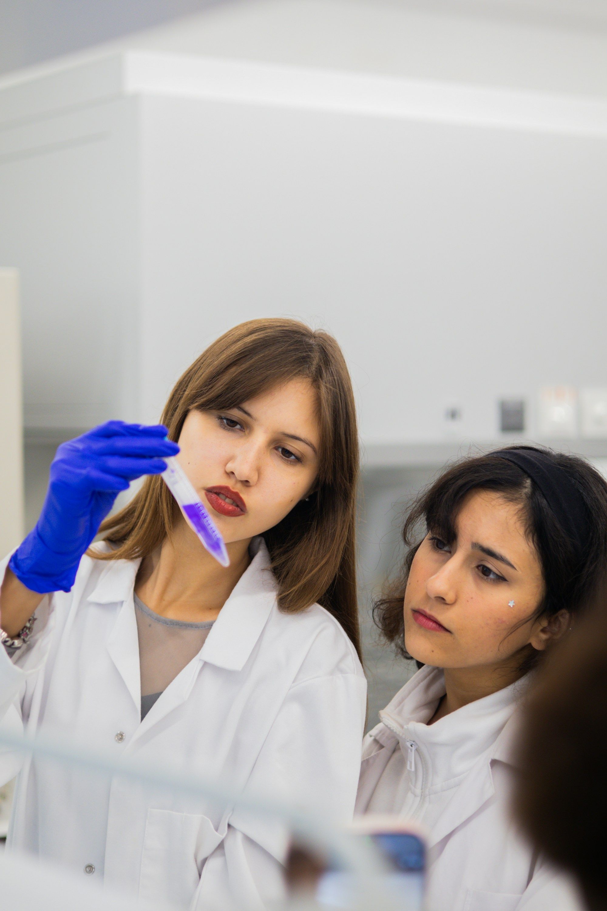 Two women in lab coats examining a purple liquid